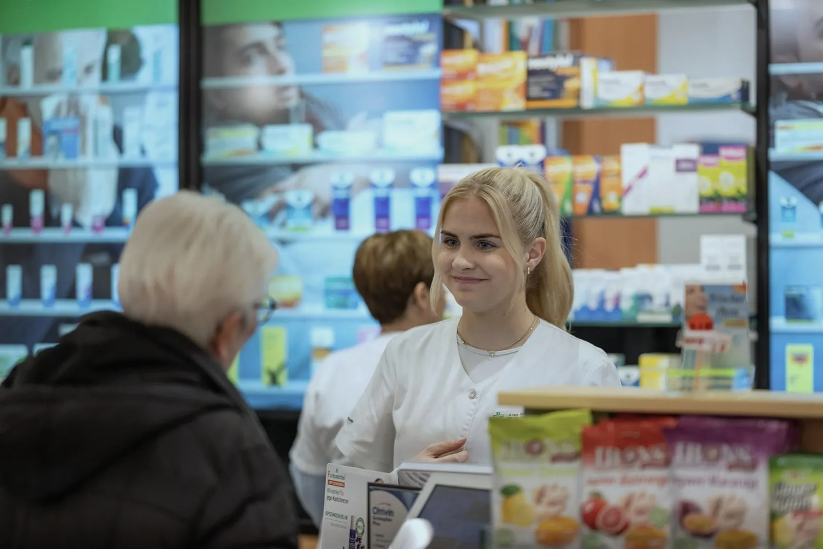 Pharma-Assistentin im Beratungsgespräch vor den interaktiven Touchscreens